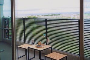 A balcony with a view of a green landscape, two tables with chairs, and a railing. - D-and Stay. 5 Resort Okinawa (Urasoe)