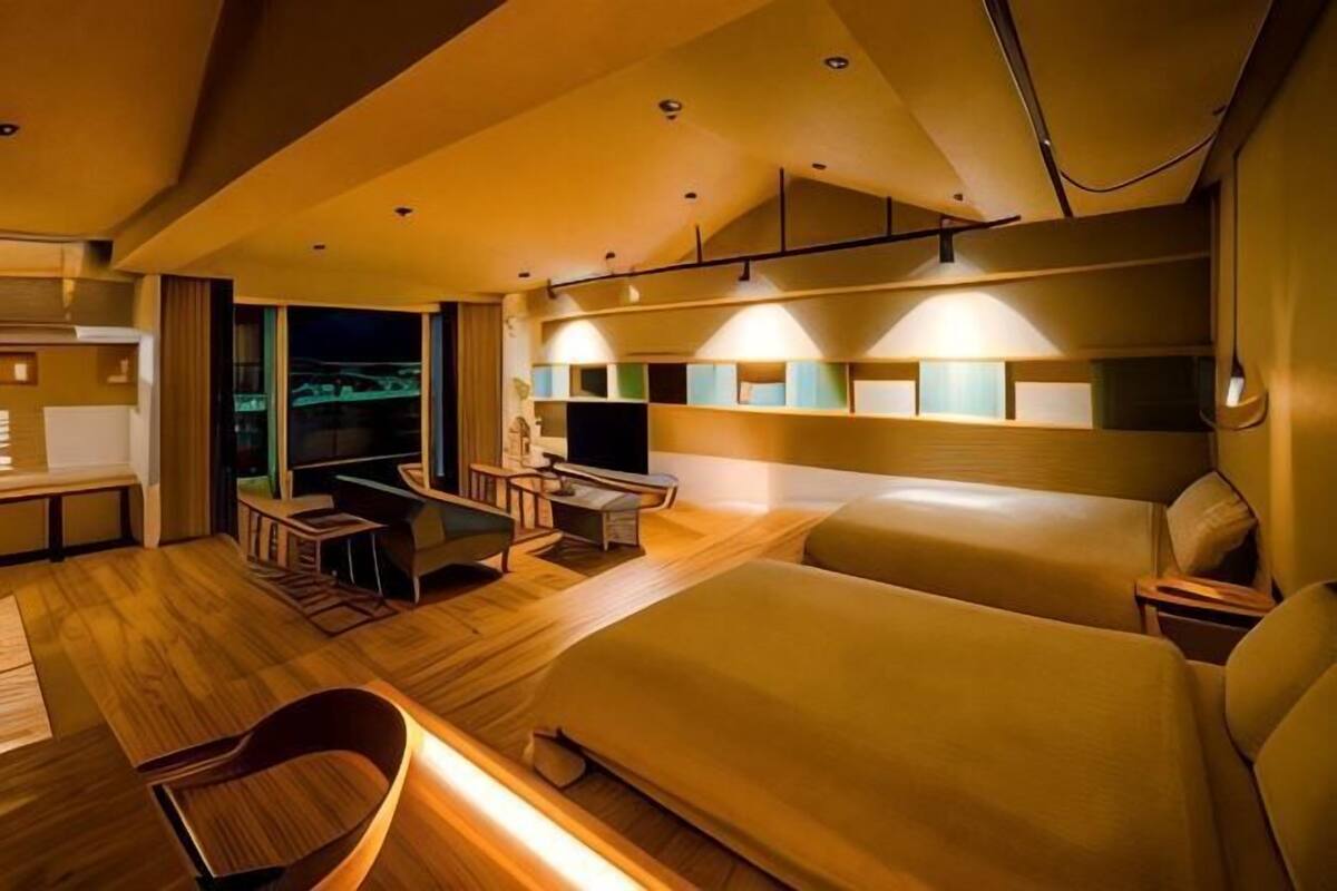 A modern hotel room with a large bed, a desk, a TV, and a balcony with a view.