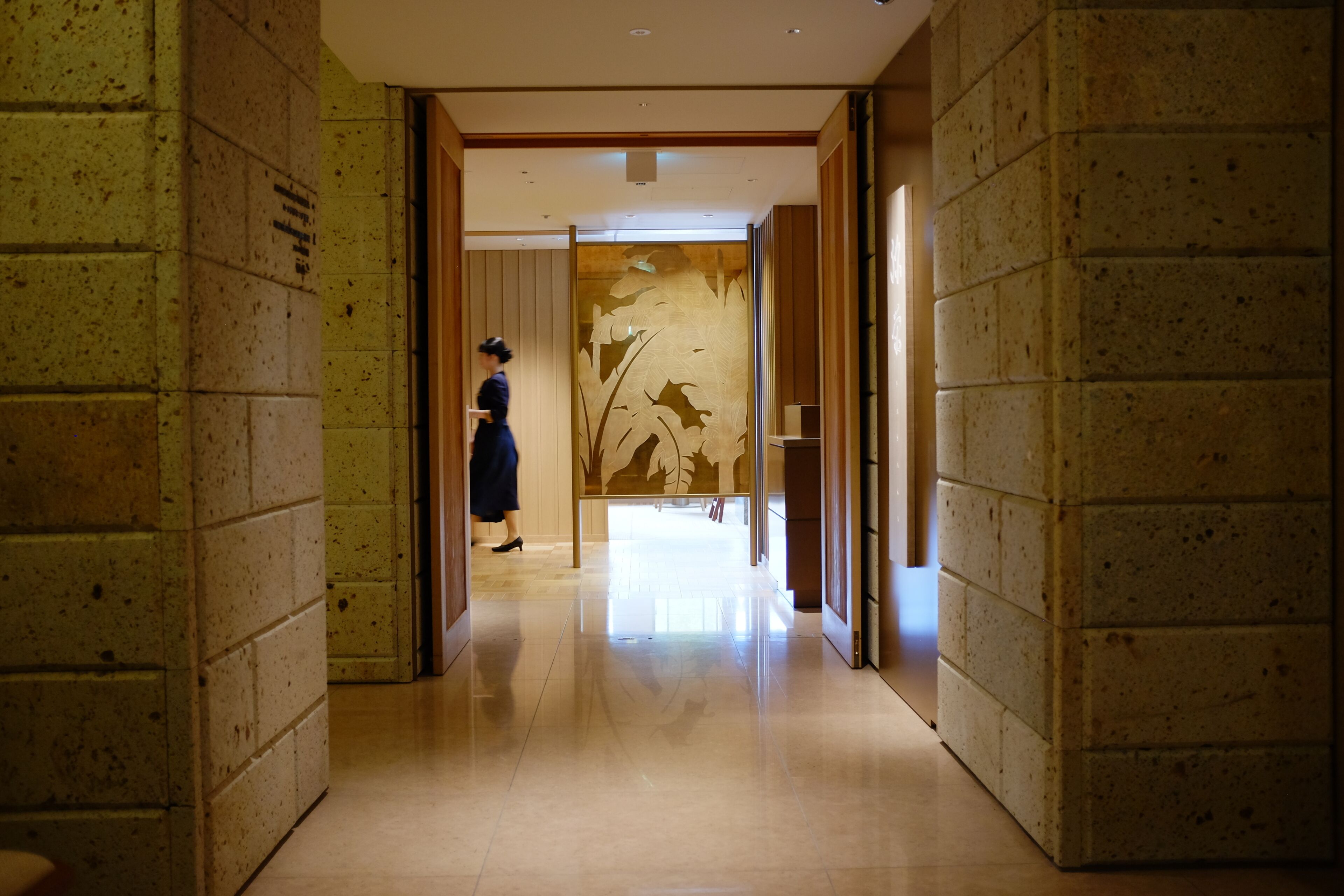 A hallway with tiled walls and a polished floor, leading to a room with a large window and a door.