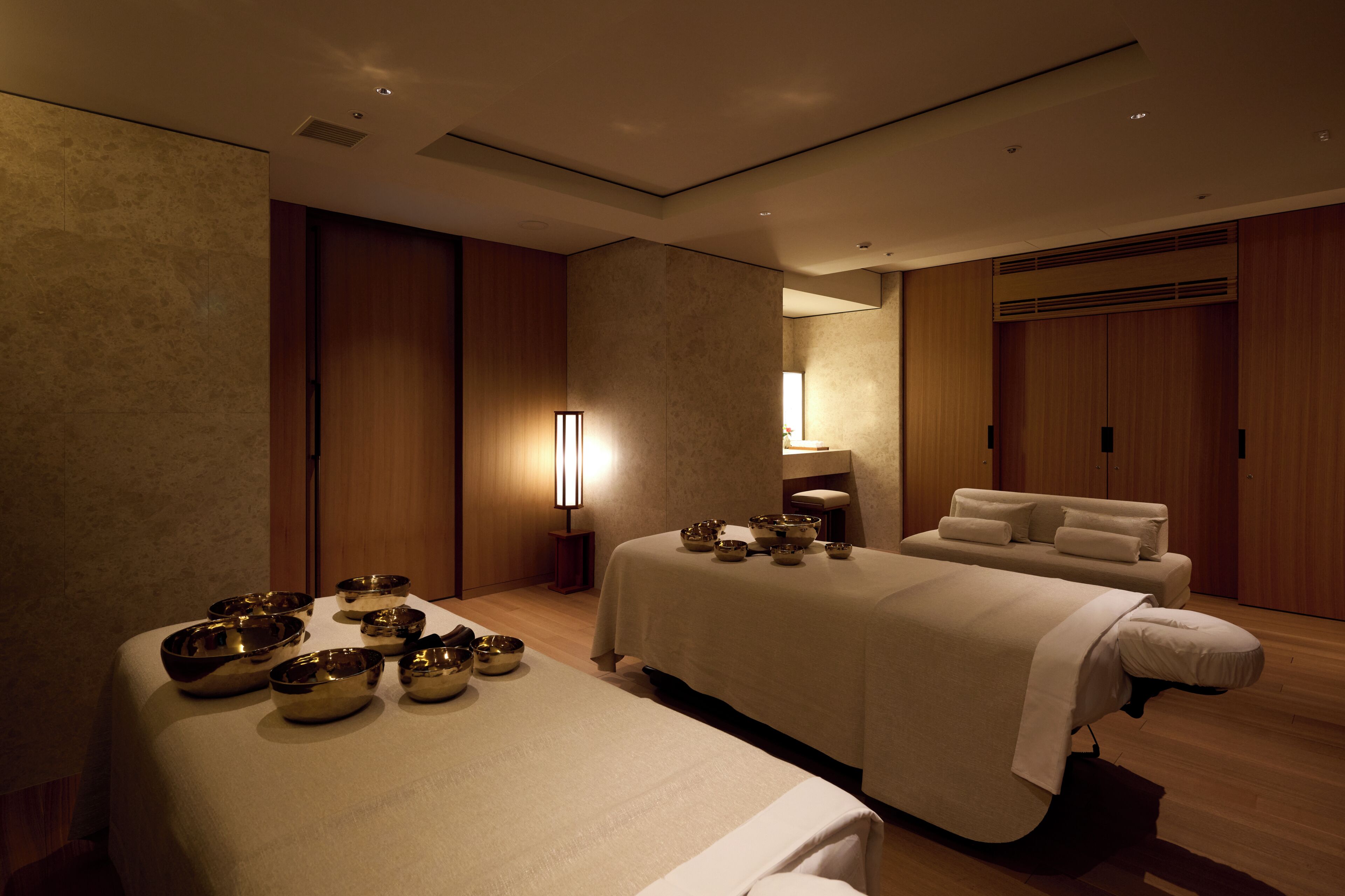 A spa room with two beds, a massage table, and several bowls on the beds.