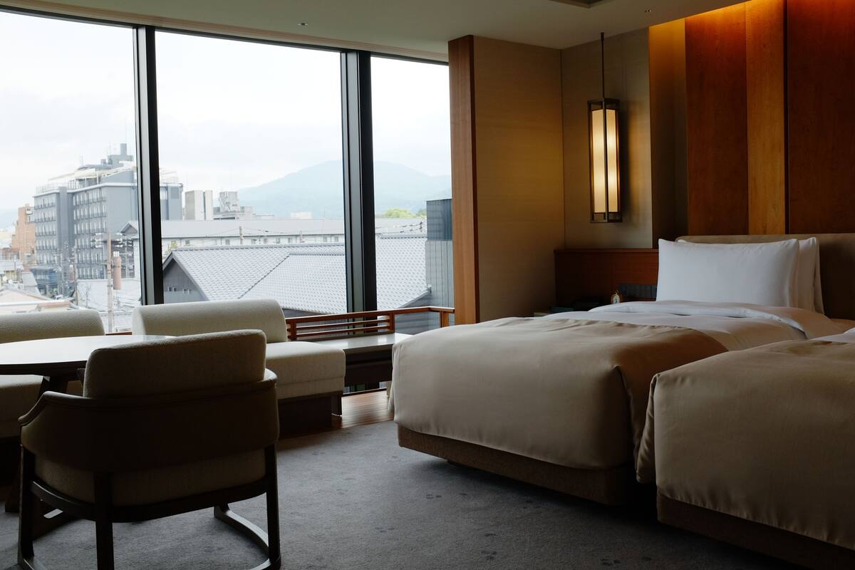 A hotel room with a large window, a bed, a desk, and a chair.