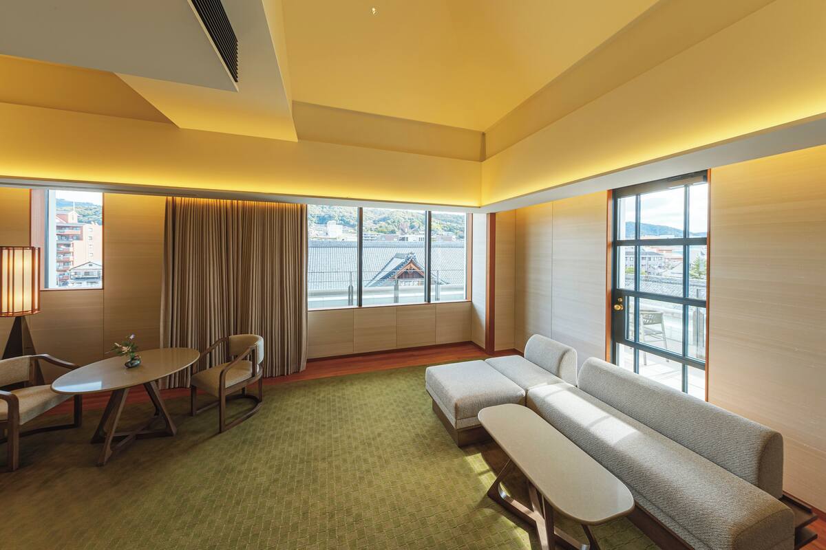 A modern hotel room with a green carpet, a sofa, a small table, and a window with curtains.