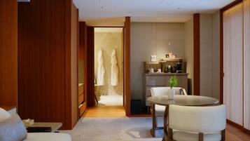 A hotel room with a wooden wardrobe, a seating area with a table and chairs, a small kitchenette, and a bathroom visible through an open door.