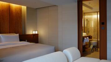 A hotel room with a bed, a sofa, a wooden panel wall, and a bathroom visible through an open door.
