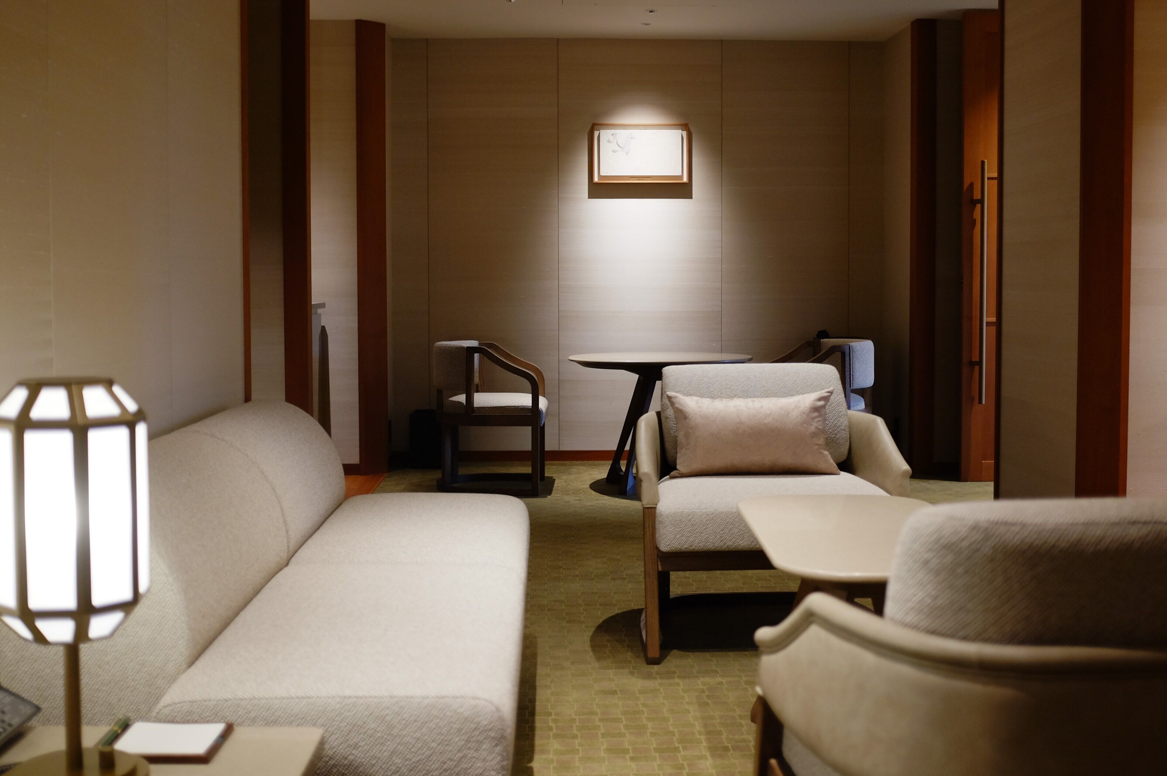 A hotel room with a sofa, a chair, a small table, and a lamp.