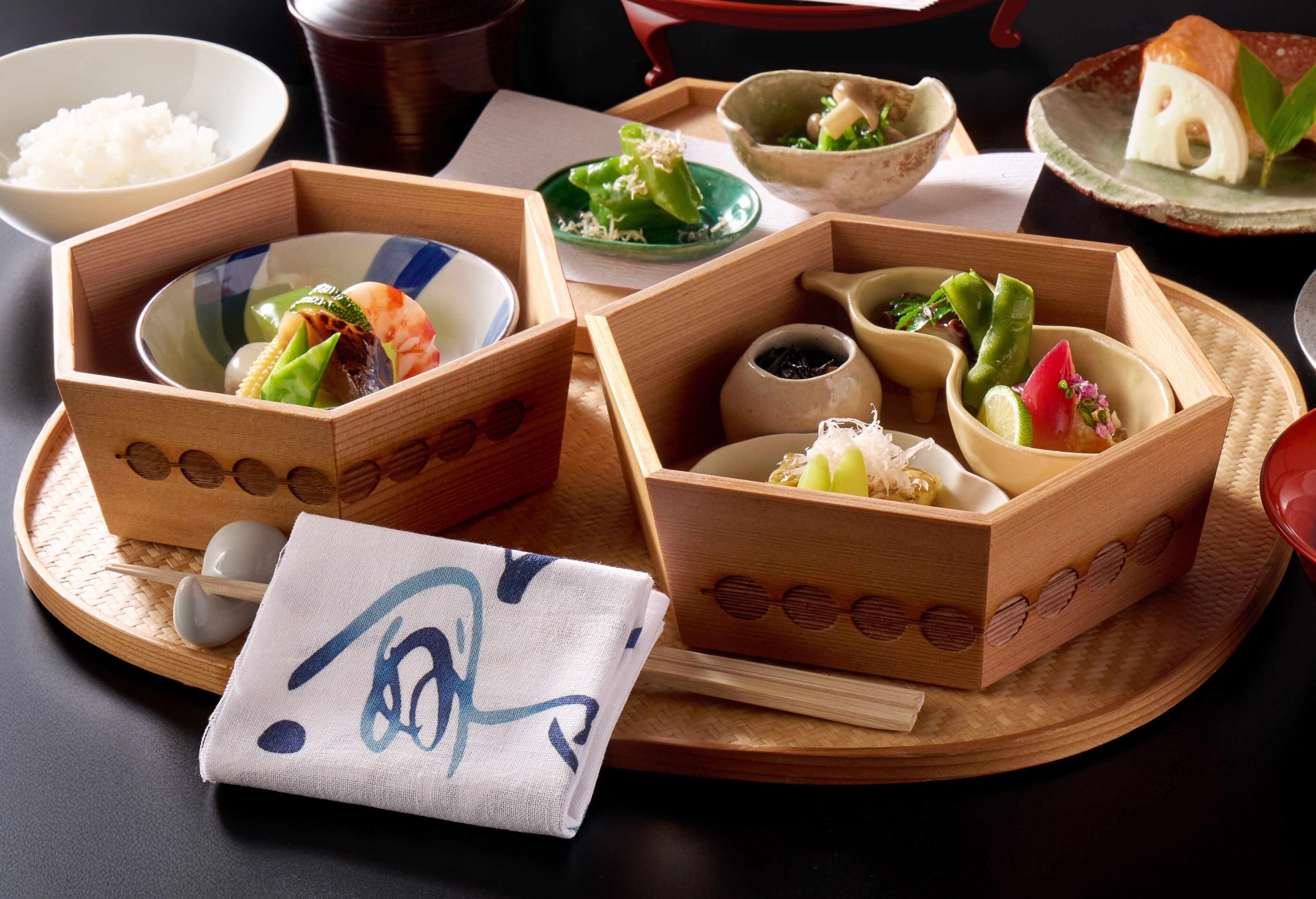 A traditional Japanese meal setup with various dishes in wooden boxes, a bowl of rice, and a napkin with a design.