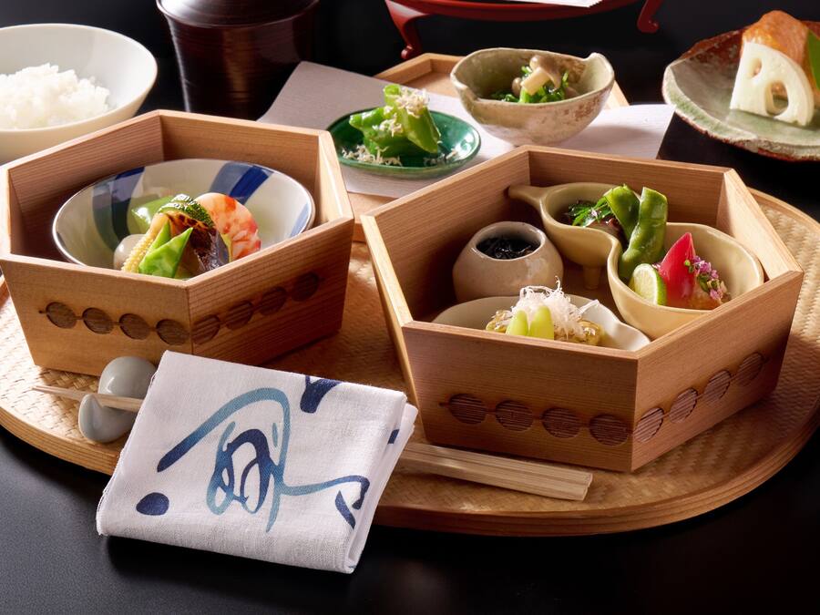 A traditional Japanese meal setup with various dishes in wooden boxes, a bowl of rice, and a napkin with a design.