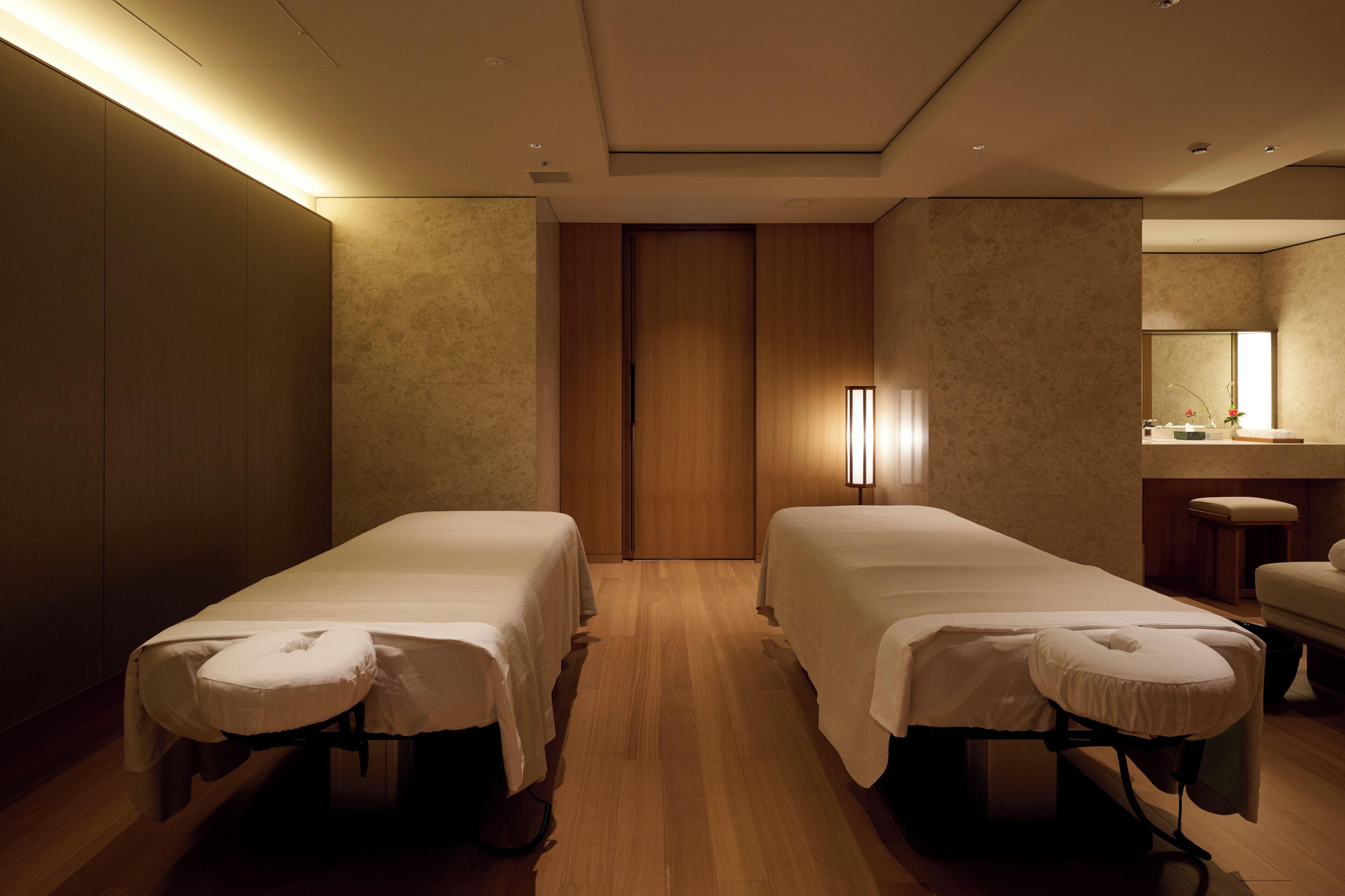 A room with two beds, a wooden floor, a mirror, and a small table.