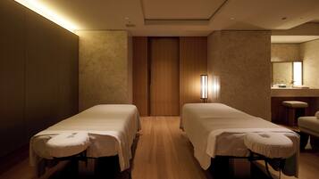 A room with two beds, a wooden floor, a mirror, and a small table.