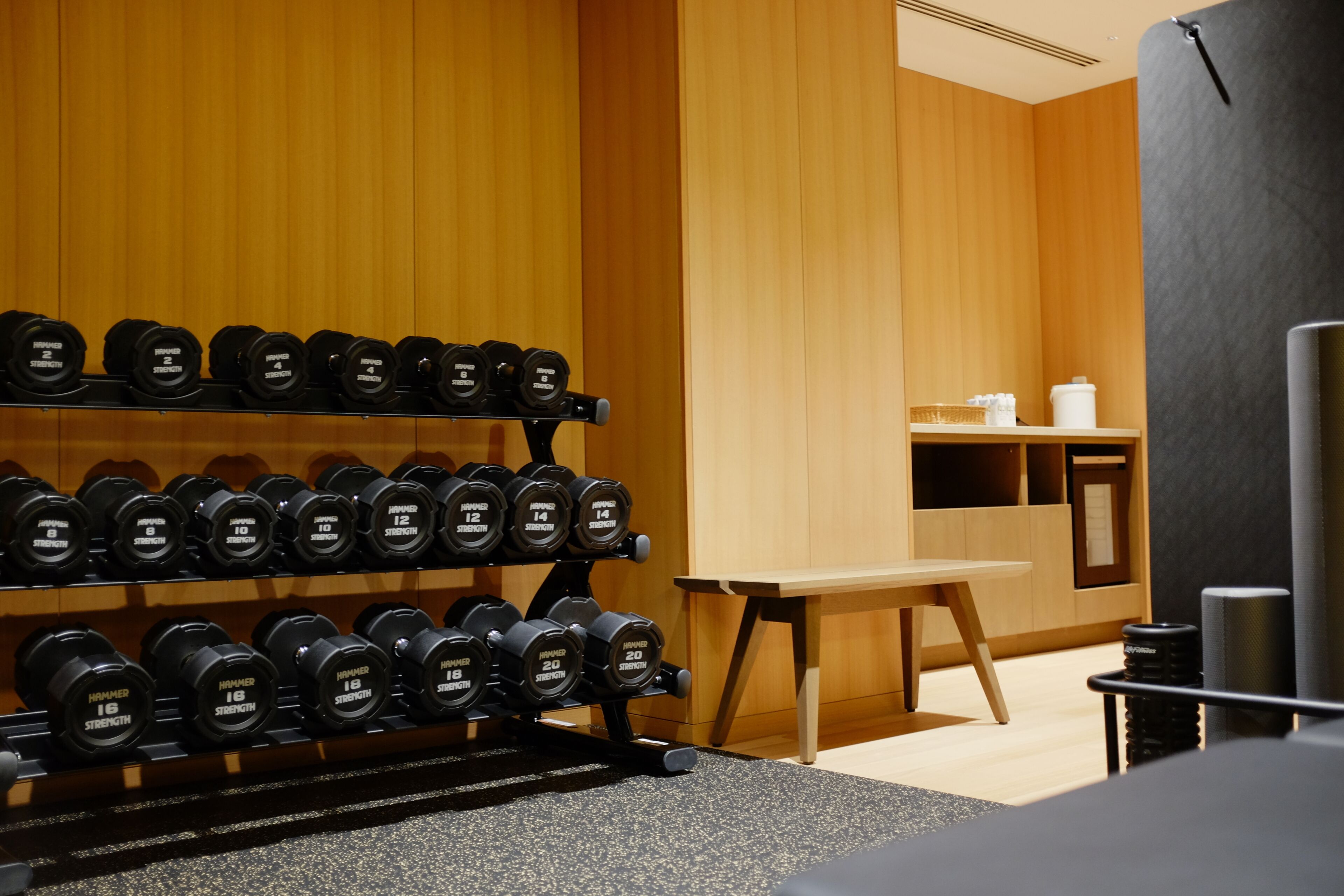 A gym with weightlifting equipment, wooden walls, and a small table with items on it.