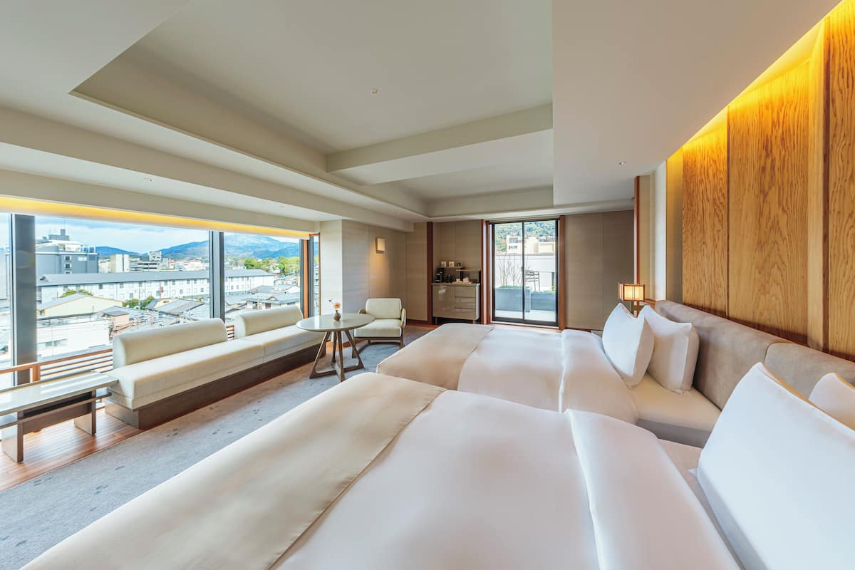 A modern hotel room with a large bed, a sofa, a small table, and a view of the city.