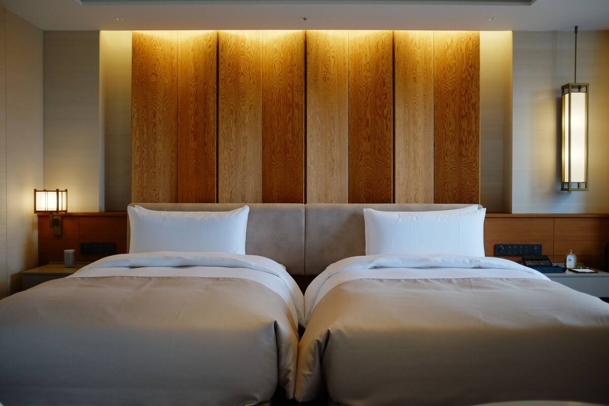 A hotel room with a large bed, a wooden headboard, a bedside table with a lamp, and a nightstand with a phone.