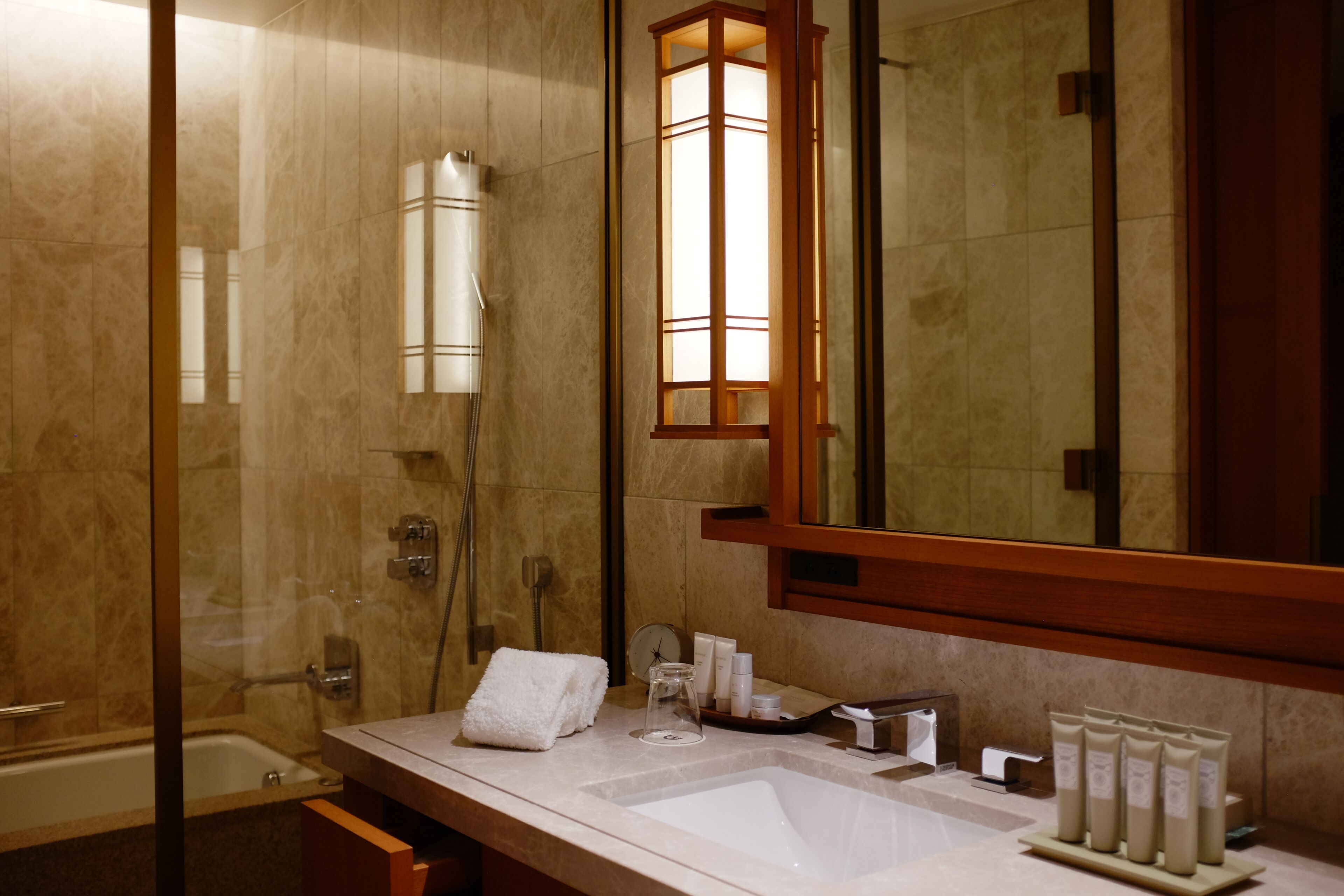 A modern bathroom with a glass-enclosed shower, a large mirror, a sink with toiletries, and a towel rack.