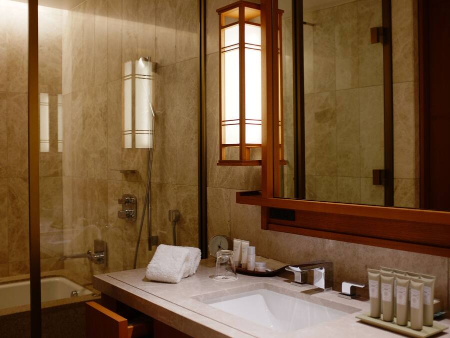 A modern bathroom with a glass-enclosed shower, a large mirror, a sink with toiletries, and a towel rack.