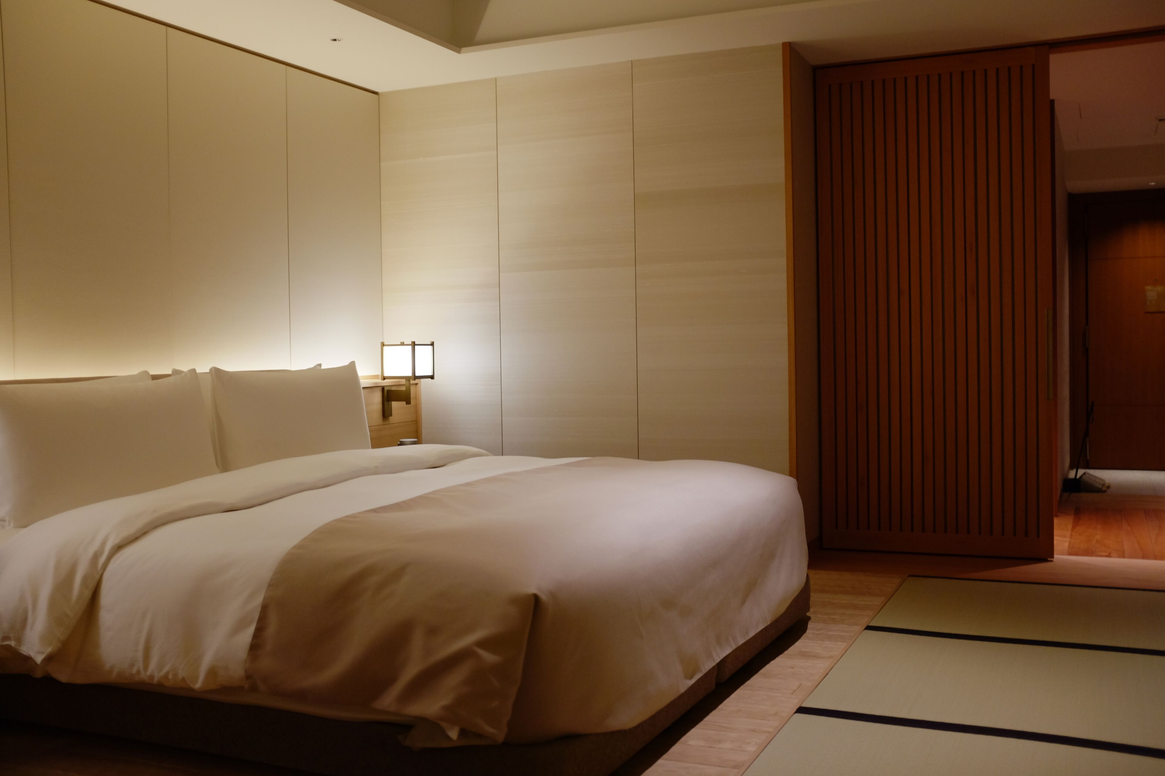 A hotel room with a large bed, a wooden wardrobe, and a nightstand with a lamp.