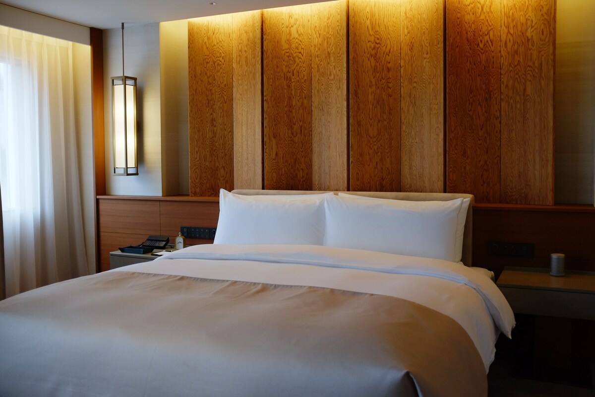 A hotel room with a large bed, a wooden headboard, a bedside table with a lamp, and a telephone.