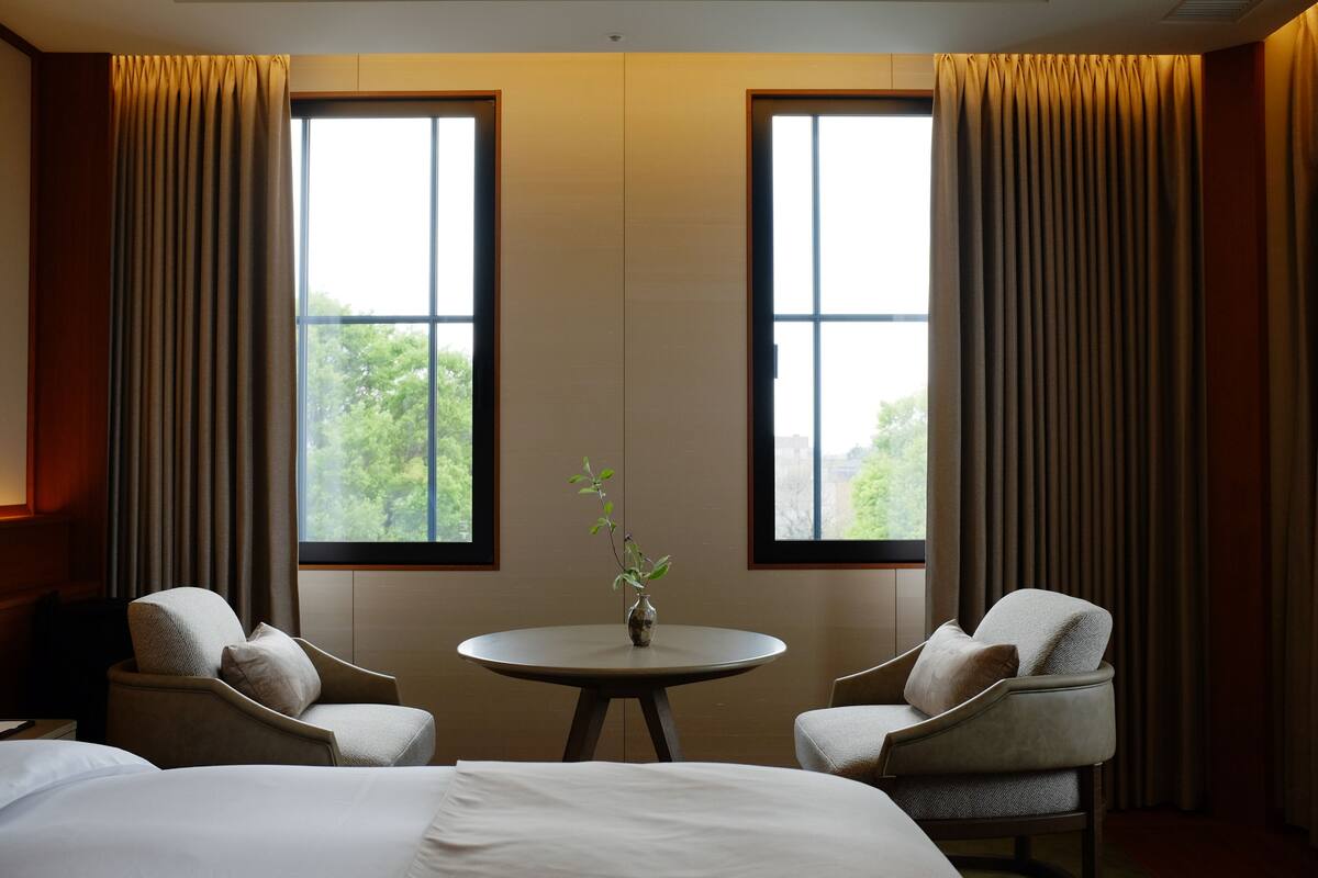 A hotel room with a bed, two armchairs, a small table, and a window with curtains.