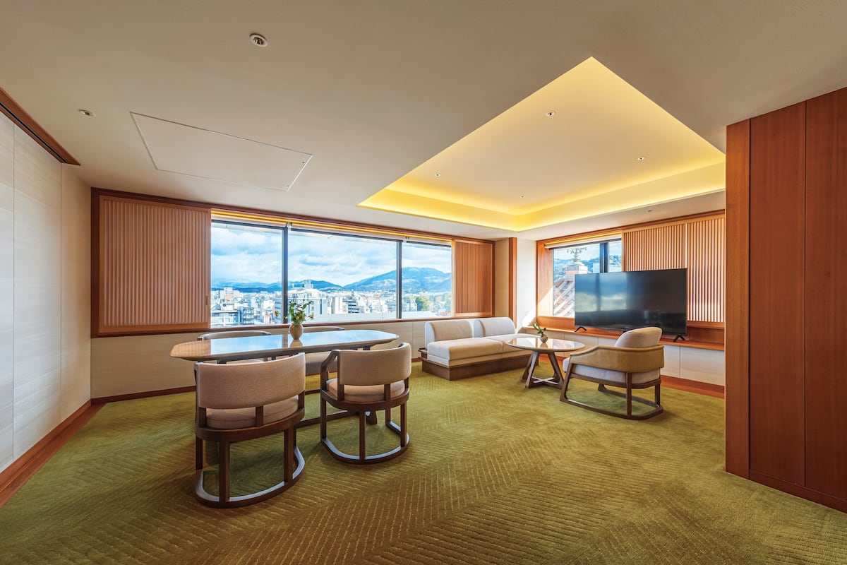A modern living room with a city view, a flat-screen TV, and a dining area with a table and chairs.