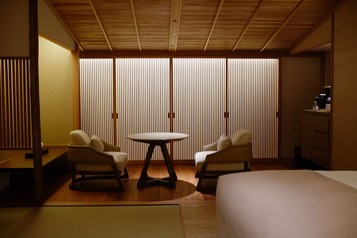 A hotel room with a bed, two armchairs, a small round table, and a sliding shoji screen.