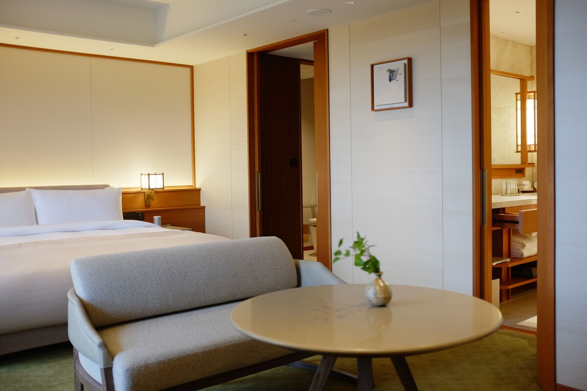 A hotel room with a bed, a sofa, a round table with a vase, and a wooden wardrobe.