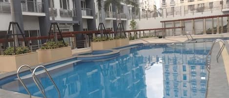 Una piscina con escalones, rodeada por un edificio con balcones y palmeras.