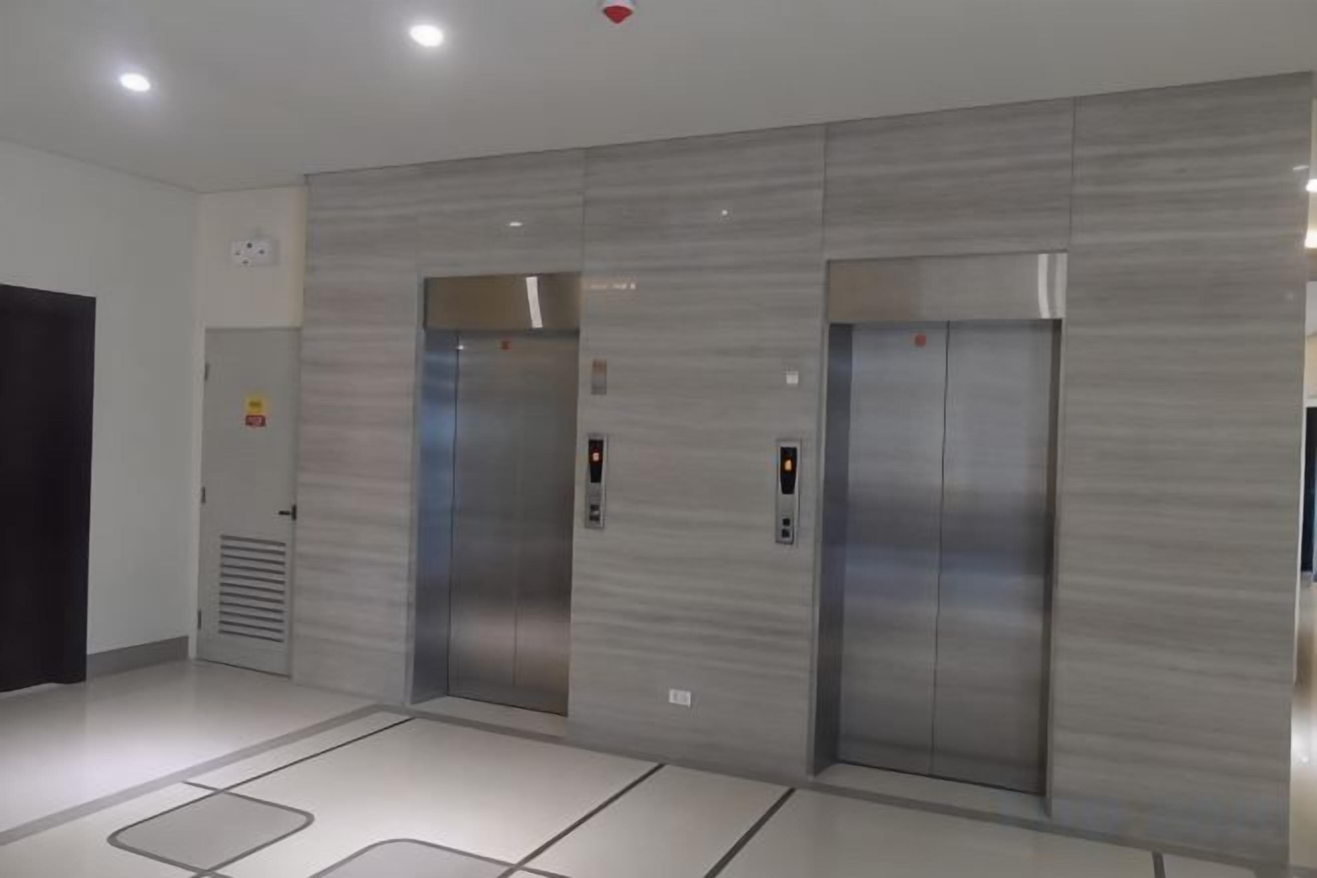 Area moderna degli ascensori con due cabine, pannelli di controllo e pavimento piastrellato.