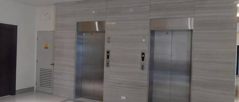 Een modern liftgedeelte met twee liften, bedieningspanelen en een betegelde vloer.