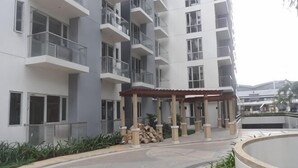 Un edificio residencial de varios pisos con balcones, una zona de estar al aire libre techada y una fuente circular.