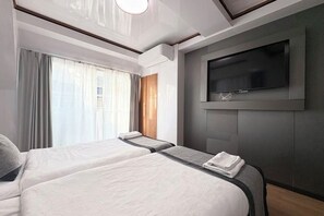 A hotel room with two beds, a TV mounted on the wall, and a window with curtains. - UenoMasakazuBuilding (Tokyo)