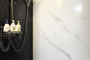 A bathroom with a black marble wall, a showerhead, and three bottles of Dove body wash on a shelf. - UenoMasakazuBuilding (Tokyo)