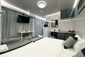 A modern hotel room with a bed, a desk, a TV, a mirror, and a kitchenette. - UenoMasakazuBuilding (Tokyo)