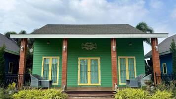 A green building with a porch, two windows with yellow trim, and a small step leading up to the entrance.