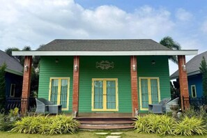 A green building with a porch, two windows with yellow trim, and a small step leading up to the entrance. - Panor Coffee House & Restaurants (Mae Chan)