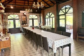 Una larga mesa de comedor con sillas, una araña y ventanas grandes con arcos.