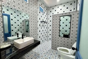 A bathroom with a white sink, black countertop, and a white toilet. The walls have a geometric patterned tile design. - Panor Coffee House & Restaurants (Mae Chan)