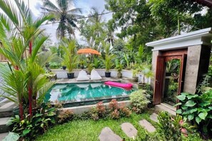 A swimming pool surrounded by lush greenery, a small structure with a door, and a pink lounge chair. - KAANAN by SEAOM Villas (Bali)