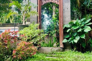 A garden with a wooden archway, various plants, and a stone structure. - KAANAN by SEAOM Villas (Bali)