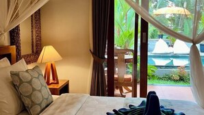 Une chambre d’hôtel avec un lit, une table de chevet avec une lampe, une chaise et une vue sur une piscine et des espaces verts.