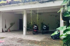 A parking area with two motorcycles, a concrete structure, and some greenery.
