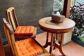 A wooden chair with an orange cushion and a small round wooden table with a woven placemat and a tissue box. - KAANAN by SEAOM Villas (Bali)