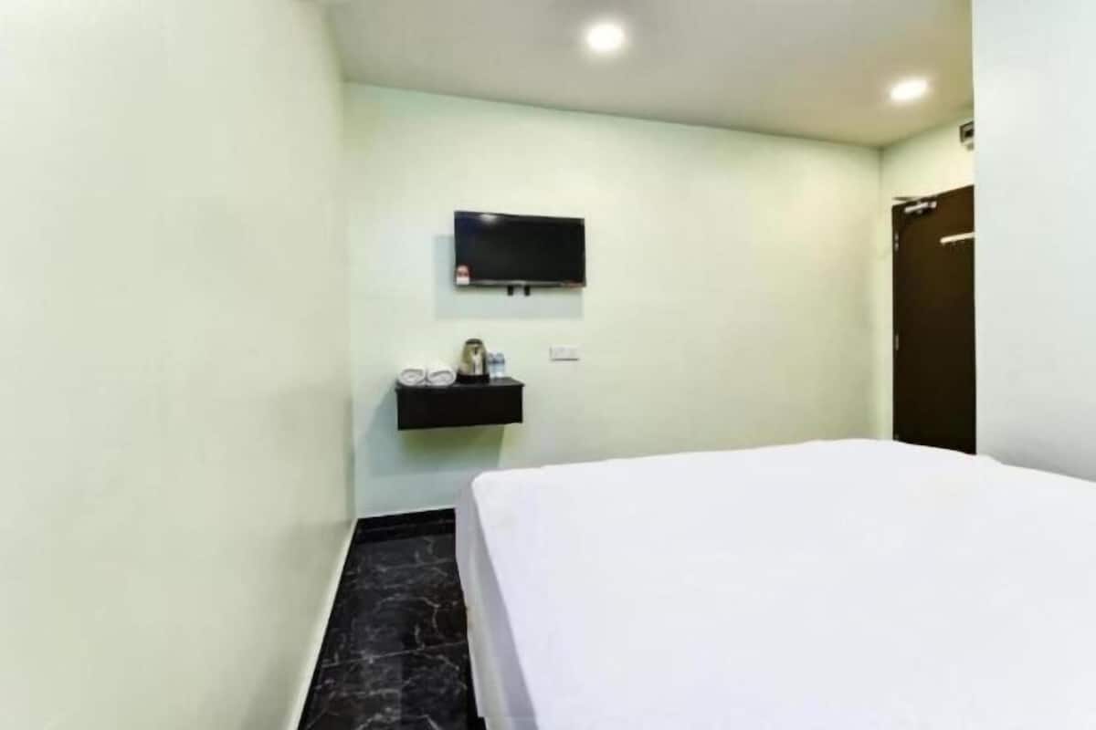 A hotel room with a bed, a TV mounted on the wall, and a small shelf with toiletries.