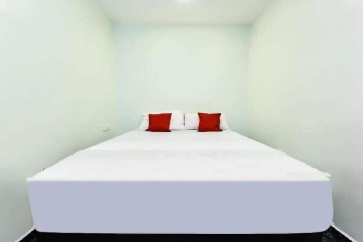 A small, single-bed room with a white bedspread and two red pillows.