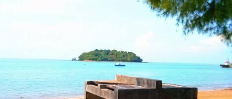 A beach with a concrete structure, a sandy shore, and a small island in the distance.