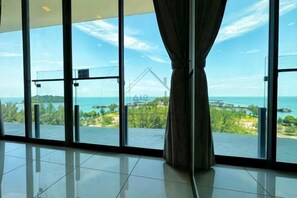 Ein Zimmer mit großen Glasfenstern, einem Vorhang und Blick auf das Meer und grüne Landschaft.