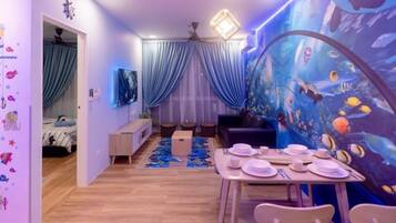 Una habitación con una mesa de comedor para cuatro personas, una cama con cortina azul, un ventilador de techo y una pared con acuario.