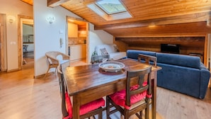 A cozy room with a wooden ceiling, a dining table with chairs, a blue sofa, and a skylight.