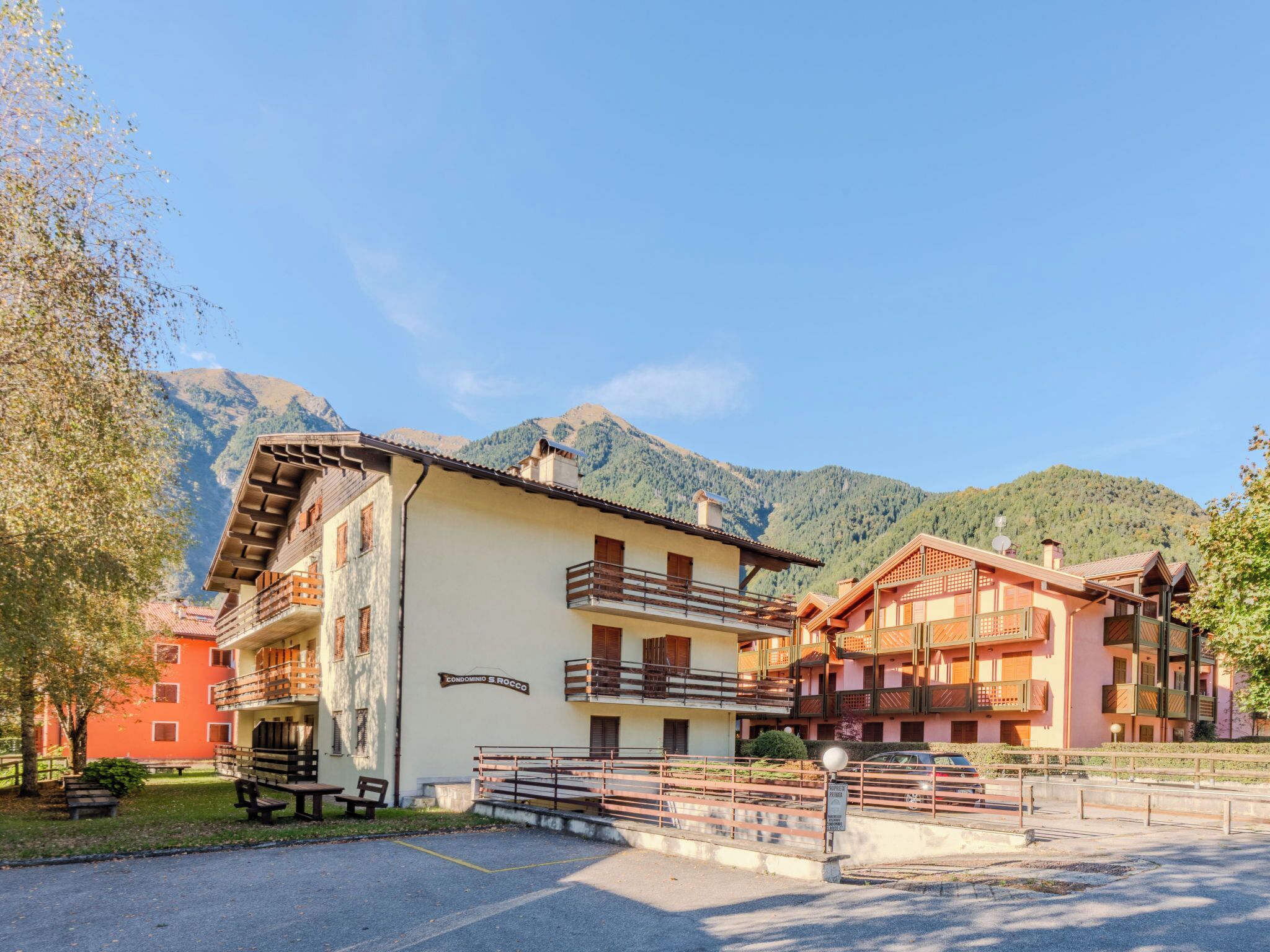 Ein Hotel mit mehreren Balkonen, einem Parkplatz und Blick auf die Berge.