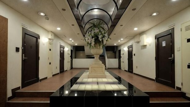 A hotel lobby with a central staircase, multiple doors, and a large vase of flowers. - TOUGAN HOTEL (Osaka)
