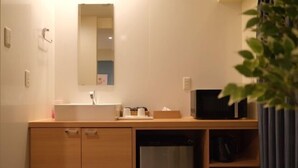 A compact hotel room with a wooden cabinet, a built-in sink, a microwave, and a small refrigerator. - TOUGAN HOTEL (Osaka)