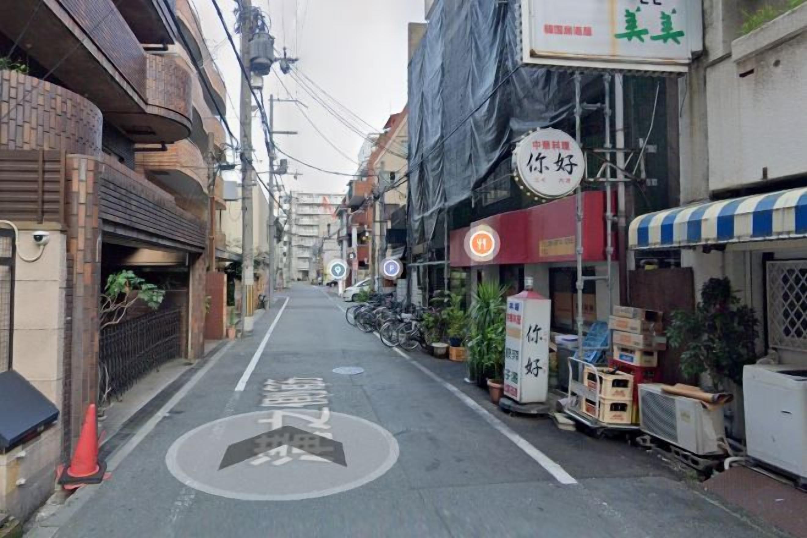 Rua estreita em área urbana, com edifícios em ambos os lados, sinalização viária bem visível e algumas motocicletas estacionadas.